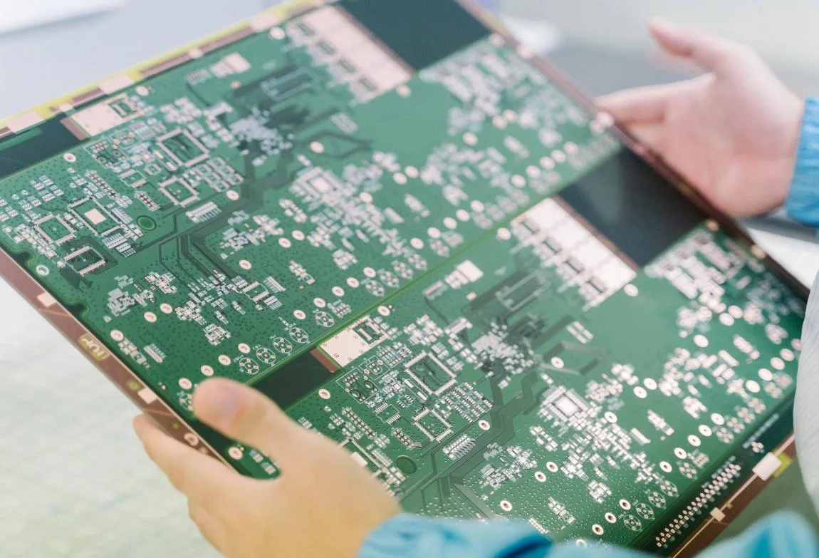 person holding a large, unpopulated green printed circuit board (PCB) panel.