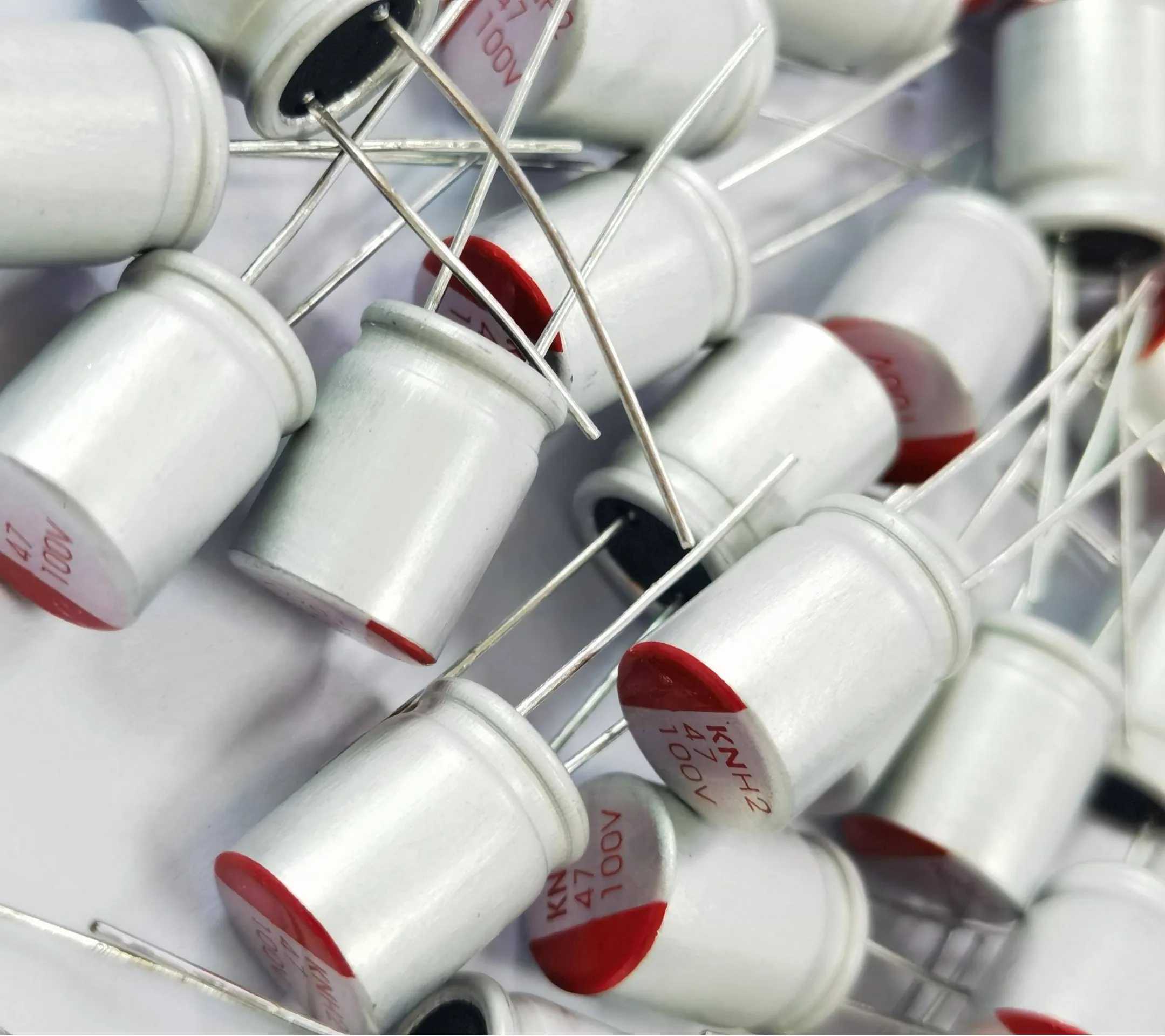 Close-up of numerous axial-leaded liquid electrolytic capacitors with white casing and red markings, showing 47 μF 100V rating