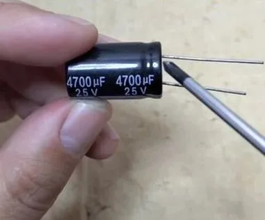 	Close-up of a large black electrolytic capacitor held between fingers, clearly showing the rating 4700 μF 25V, used for power supply filtering and quality check.