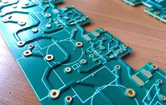Blue-green printed circuit boards with white circuit traces and solder pads laid on a wooden surface close-up.